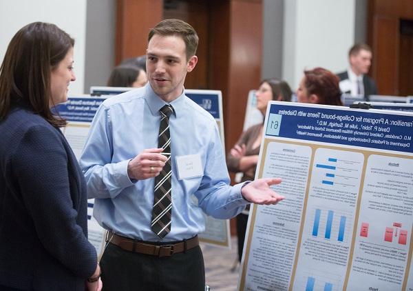 An M4 presents his research poster to a 教员 at the annual Capstone Colloquium